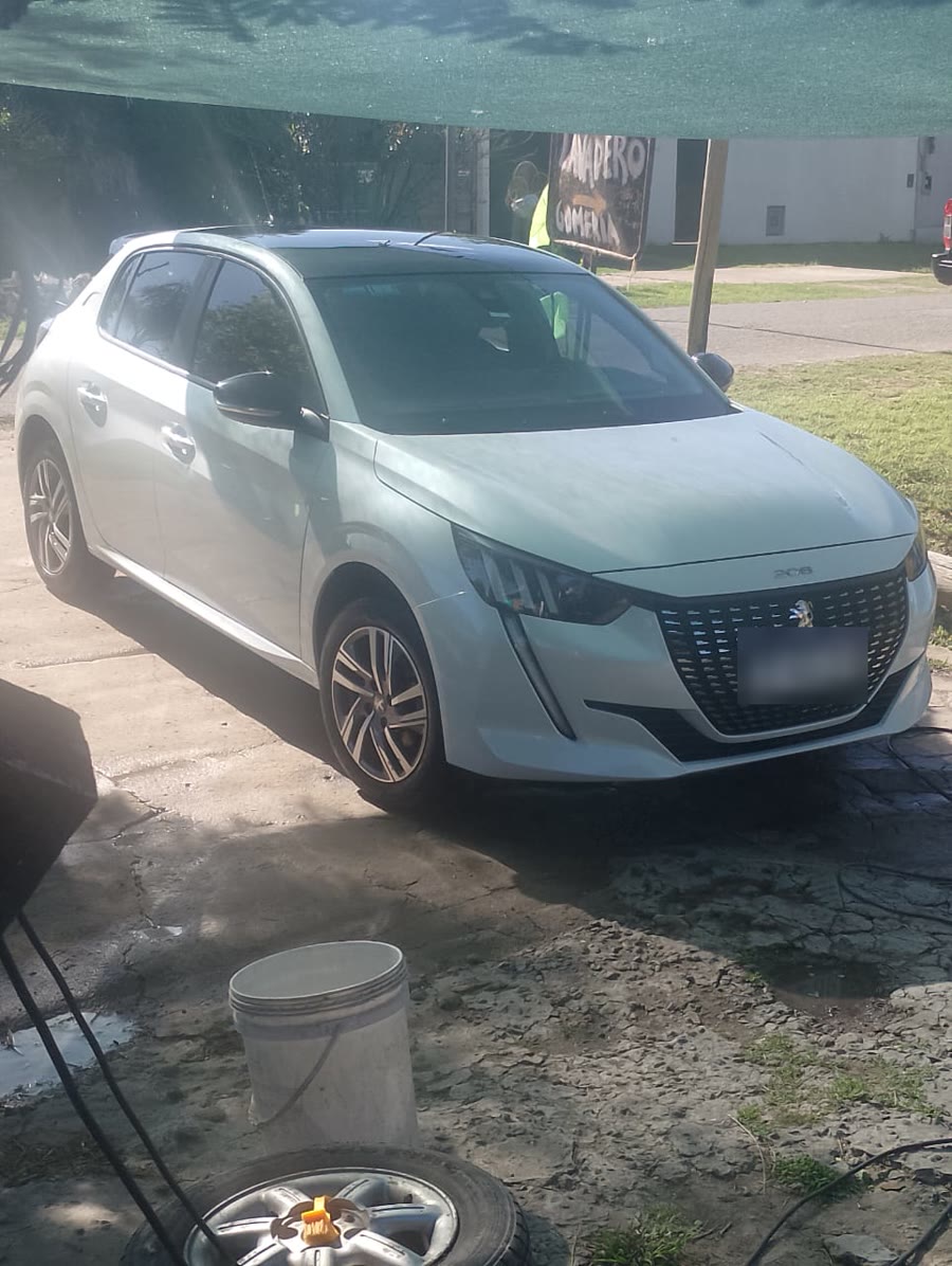 Un Peugeot 208 blanco recién lavado, con el cartel del taller atrás